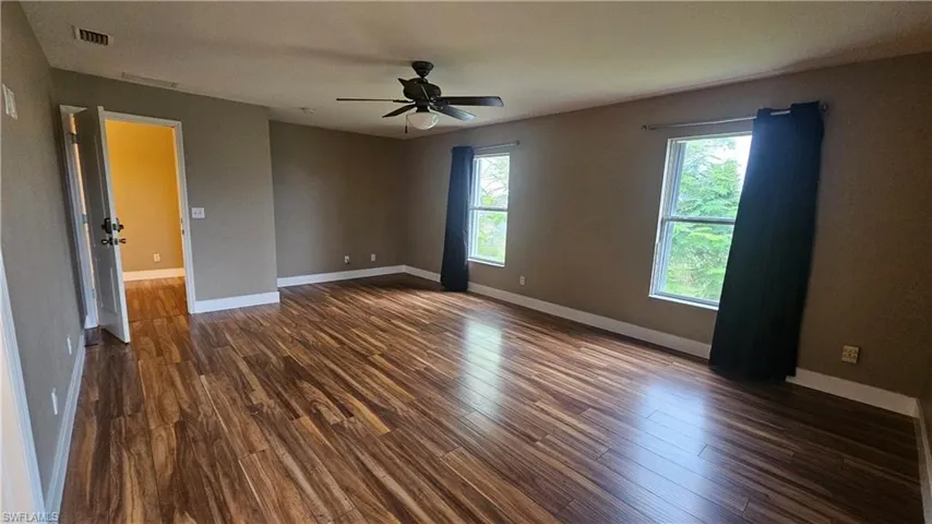 Empty room with ceiling fan, dark hardwood / wood-style flooring, and a wealth of natural light