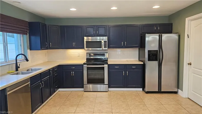 Kitchen with sink, blue cabinetry, appliances with stainless steel finishes, tasteful backsplash, and light tile patterned flooring