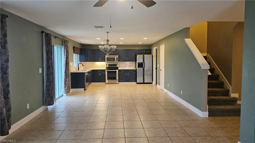 Kitchen with ceiling fan with notable chandelier, stainless steel appliances, sink, light tile patterned floors, and pendant lighting