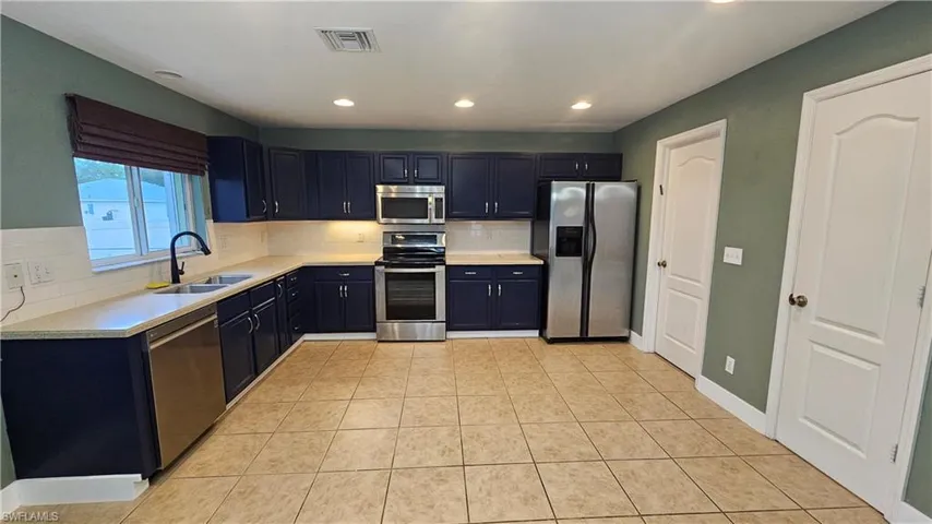 Kitchen with backsplash, sink, light tile patterned floors, and appliances with stainless steel finishes
