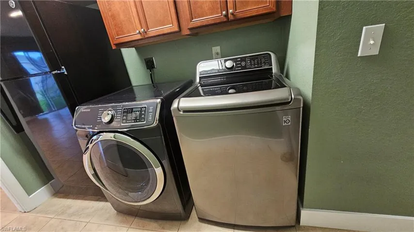 Laundry room with cabinets, light tile patterned flooring, and washing machine and clothes dryer