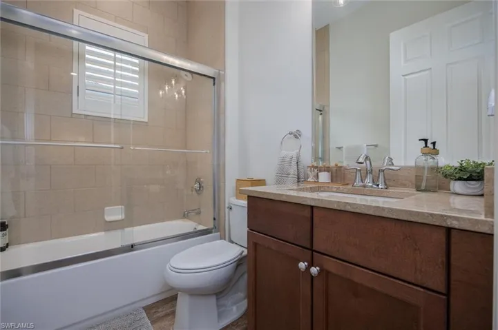 Bathroom featuring a tub and shower combination with glass enclosure, beige wall tiling, and a window with plantation shutters