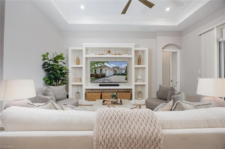 Living area featuring a tray ceiling with a ceiling fan, recessed lighting, and a built-in entertainment center with open shelving and storage baskets