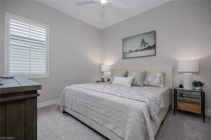 Bedroom featuring light gray walls, patterned carpeting, a ceiling fan, and window with plantation shutters
