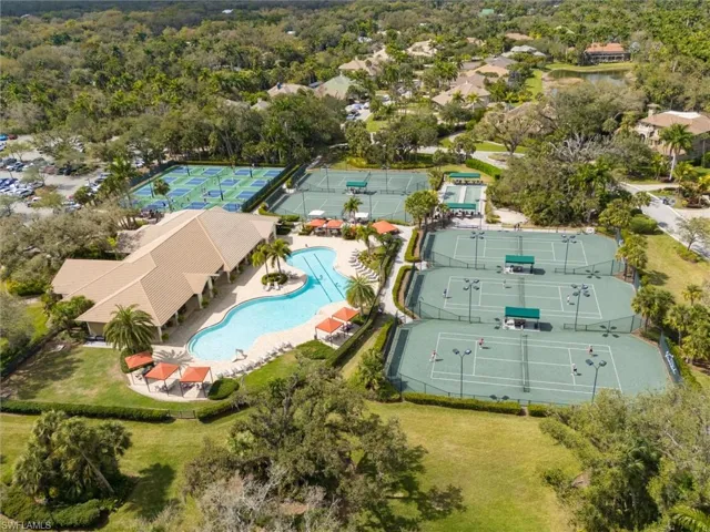 Community amenities featuring a large clubhouse with a tiled roof, a freeform swimming pool, multiple tennis courts, and several pickleball courts, all surrounded by mature landscaping and residential properties