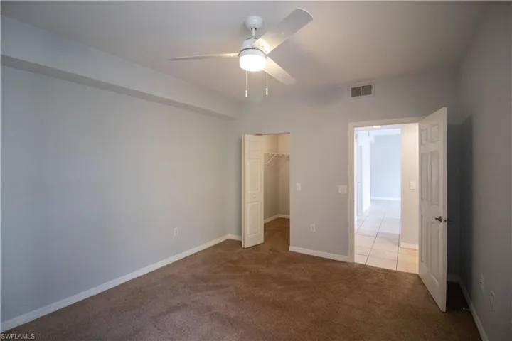 Unfurnished bedroom featuring a closet, a walk in closet, ceiling fan, and light colored carpet