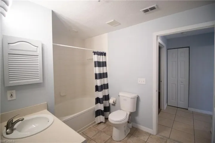 Full bathroom with tile patterned flooring, shower / bathtub combination with curtain, a textured ceiling, toilet, and vanity