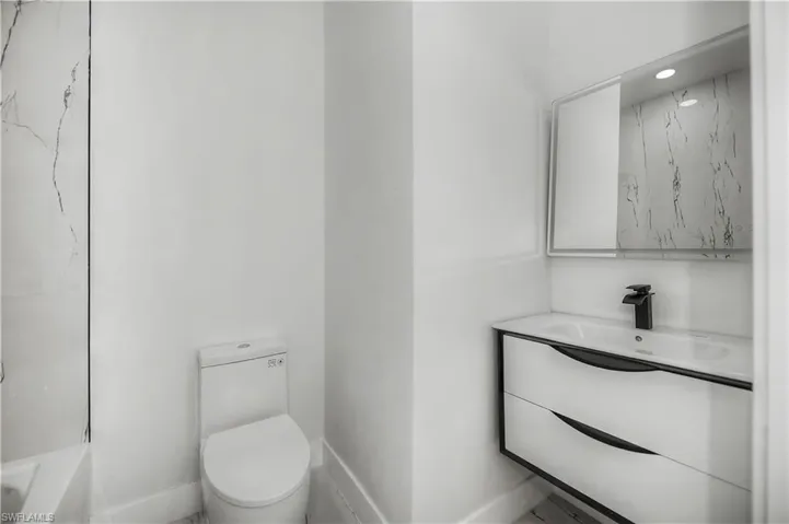 Bathroom featuring a floating vanity with integrated sink, black hardware, wall-mounted mirror, and a white toilet