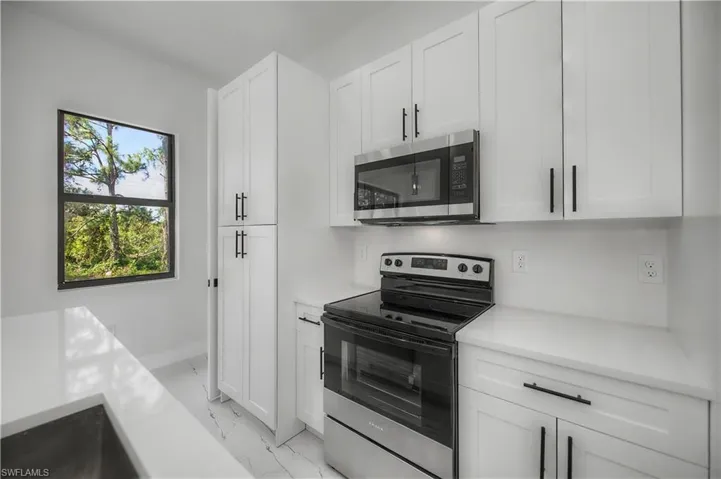 Modern kitchen featuring white shaker cabinetry, stainless steel appliances, white countertops, and wood-finish flooring