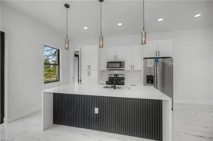Kitchen featuring white cabinetry, stainless steel appliances, a center island with a sink, pendant lighting, and white tile flooring