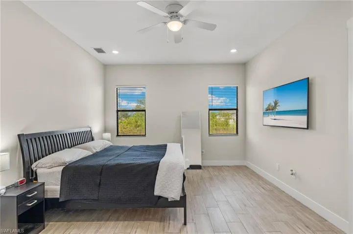 Bedroom with ceiling fan, light wood-type flooring, and multiple windows