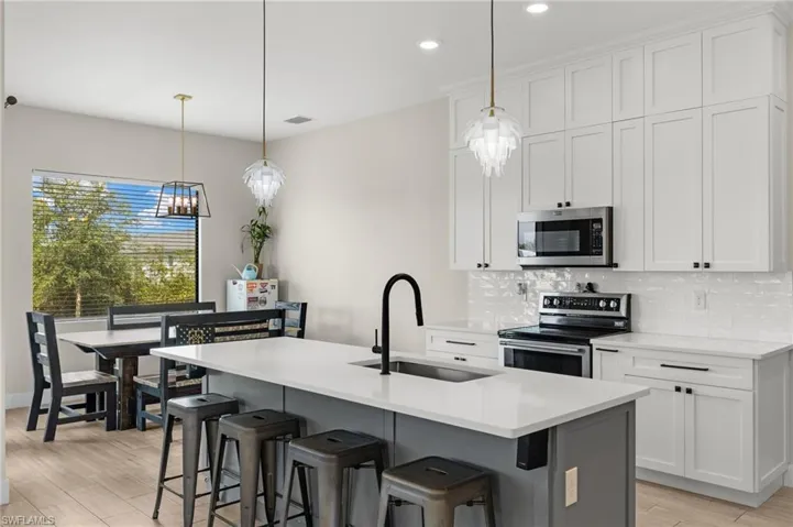 Kitchen with stainless steel appliances, white cabinets, a center island with sink, and sink