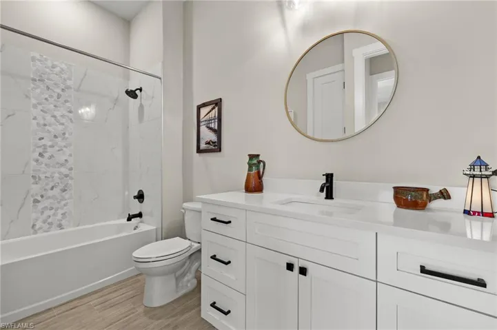 Full bathroom with hardwood / wood-style flooring, tiled shower / bath combo, vanity, and toilet