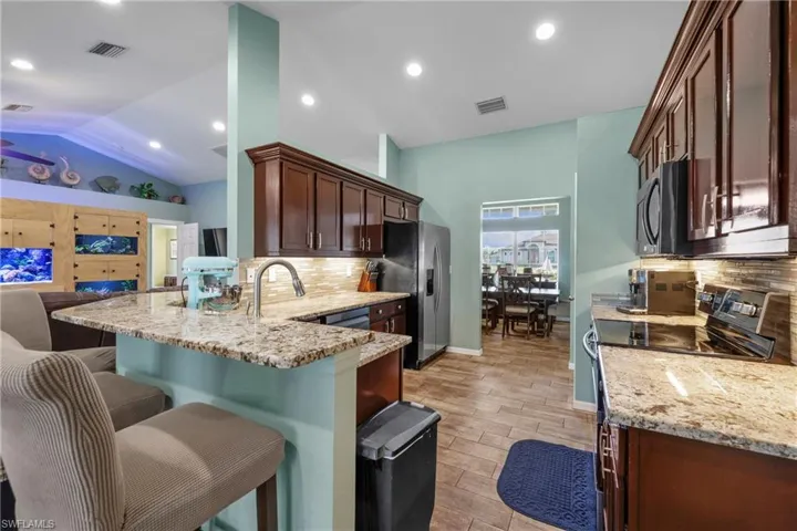 Kitchen with sink, light stone counters, vaulted ceiling, kitchen peninsula, and stainless steel appliances