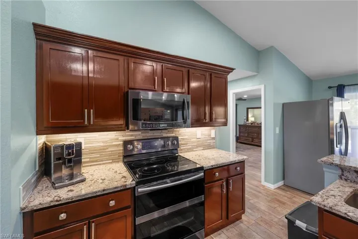 Kitchen featuring lofted ceiling, stainless steel appliances, light stone counters, decorative backsplash, and light wood-type flooring