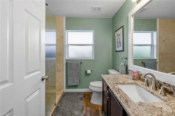 Bathroom featuring vanity, toilet, wood-type flooring, and a tile shower