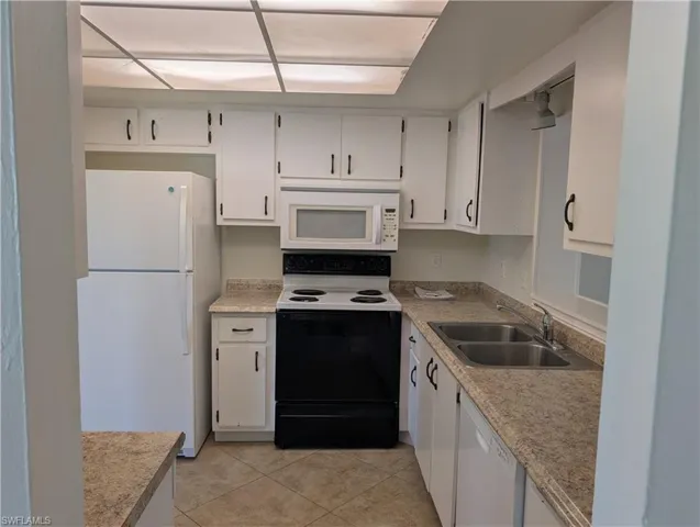 Kitchen with white appliances, light countertops, white cabinets, a sink, and light tile patterned flooring