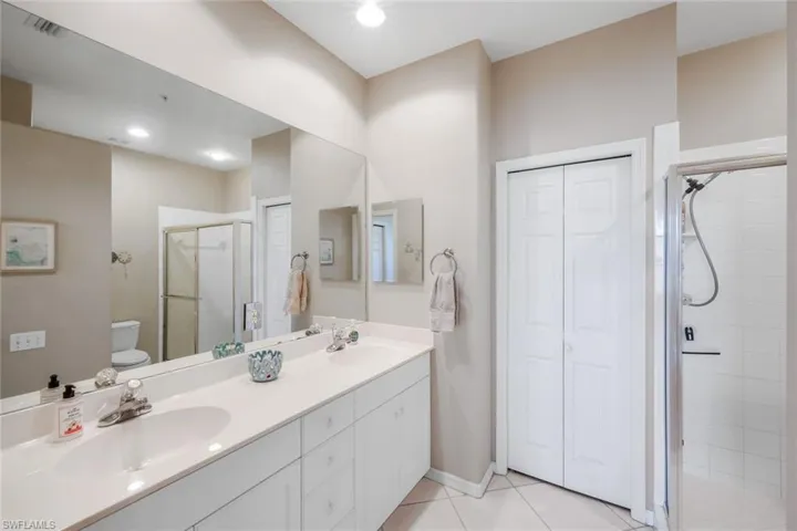 Bathroom featuring a closet, double vanity, light tile patterned floors, a stall shower, and recessed lighting