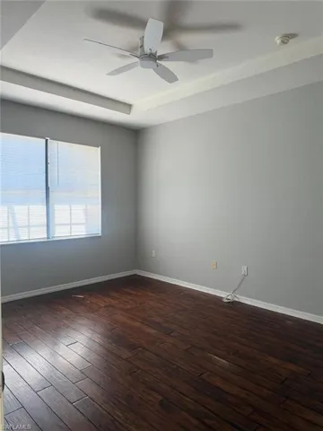 Room featuring dark hardwood flooring, light grey walls, and a white ceiling fan