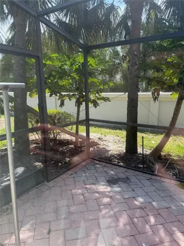 The property features a screened-in patio area with brick pavers, surrounded by palm trees and lush greenery
