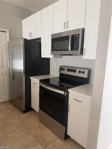 Kitchen featuring white shaker-style cabinetry, stainless steel appliances, light-colored countertops, and tiled flooring