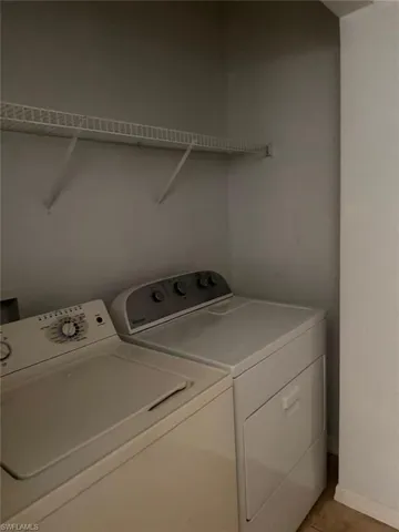 Dedicated laundry area featuring a washer, a dryer, and a wall-mounted wire shelf