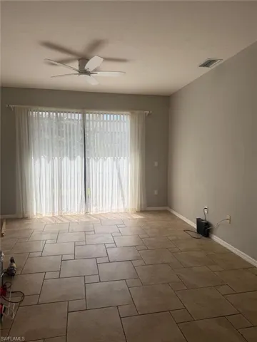 This room features patterned tile flooring, a ceiling fan, and sliding glass doors with vertical blinds