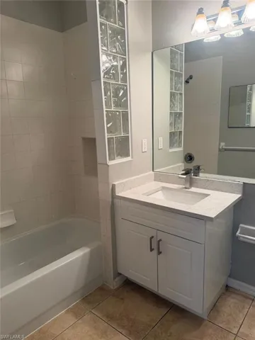 The bathroom features a vanity with a white countertop and a rectangular sink, a bathtub with white tiled walls, and a decorative glass block partition