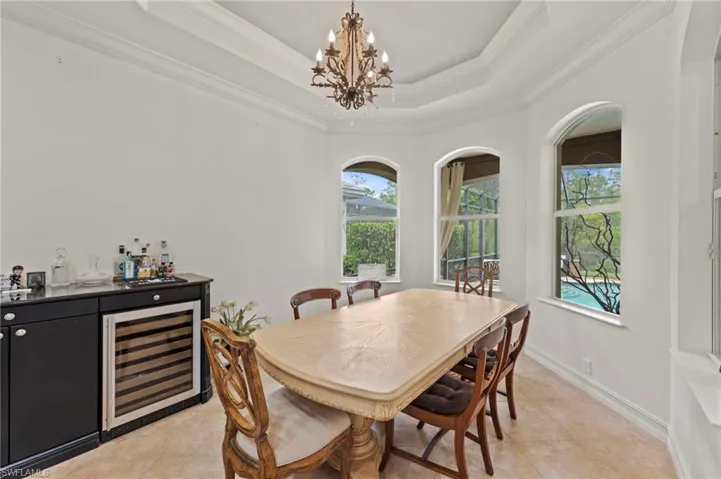 Dining room with a raised ceiling, beverage cooler, a chandelier, ornamental molding, and light tile patterned floors