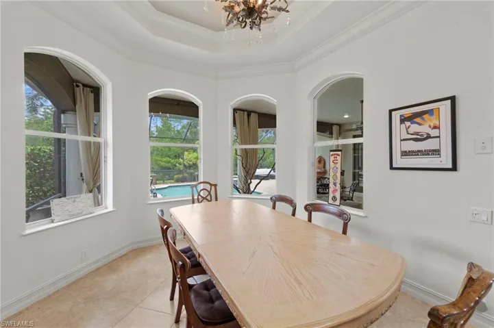 Dining area featuring a tray ceiling, a chandelier, light tile patterned flooring, and ornamental molding