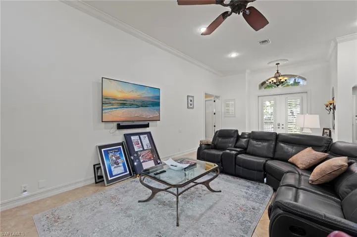 Living room with crown molding, a ceiling fan, french doors, light tile patterned floors, and a chandelier