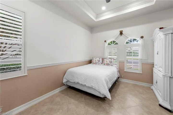 Bedroom featuring a tray ceiling, crown molding, light tile patterned floors, ceiling fan, and recessed lighting