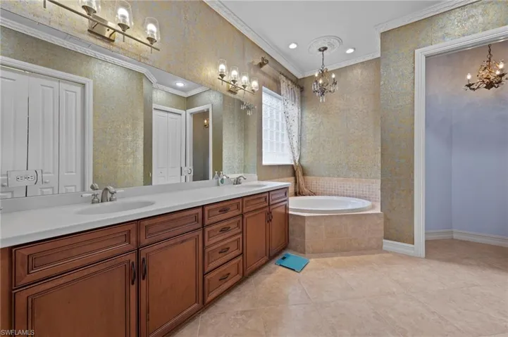 Full bathroom with a garden tub, double vanity, wallpapered walls, light tile patterned floors, and a chandelier