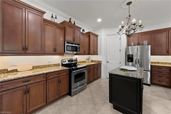 Kitchen with stainless steel appliances, light stone counters, pendant lighting, crown molding, and a kitchen island