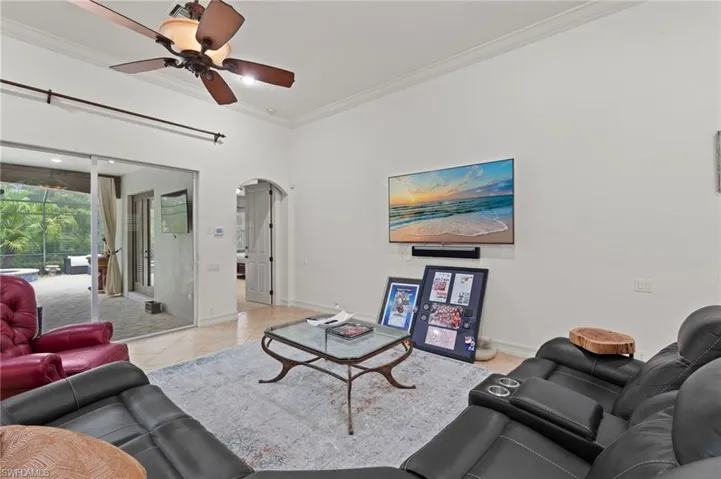 Living room featuring ornamental molding, arched walkways, light tile patterned floors, and a ceiling fan