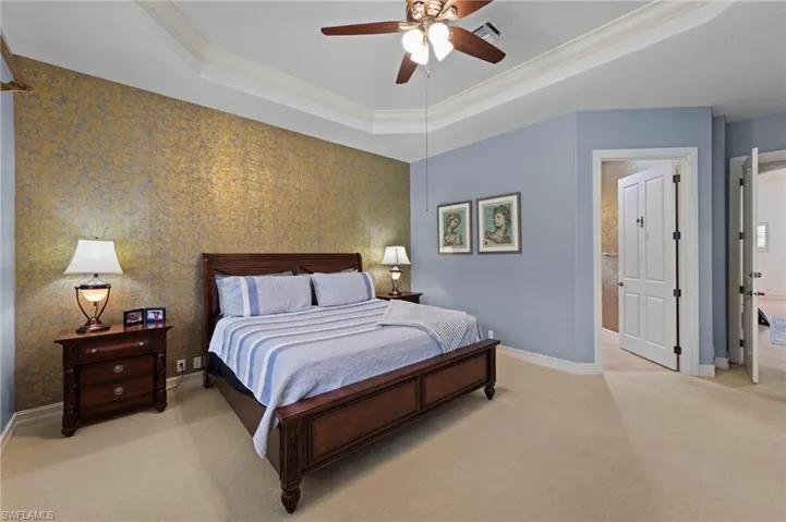 Bedroom with light carpet, a raised ceiling, ornamental molding, a ceiling fan, and ensuite bathroom