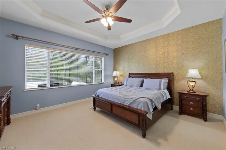 Bedroom with wallpapered walls, a raised ceiling, light carpet, ornamental molding, and ceiling fan