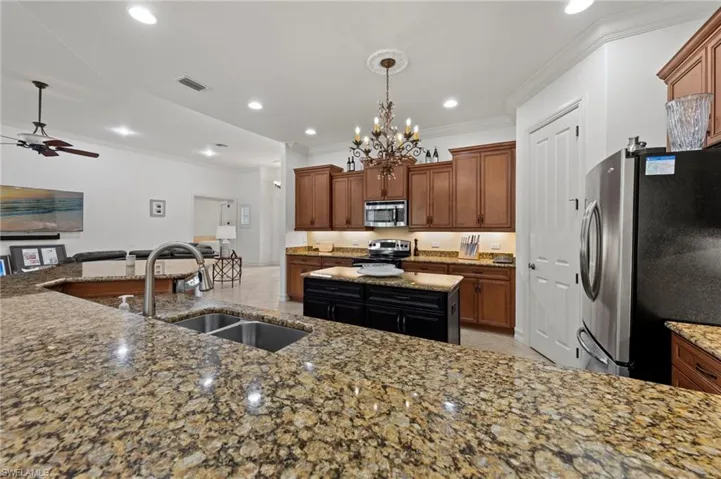Kitchen with ornamental molding, stainless steel appliances, brown cabinets, light stone countertops, and decorative light fixtures
