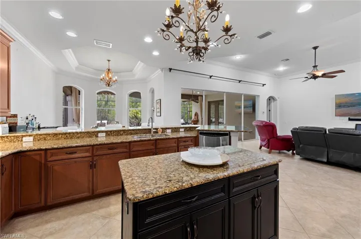 Kitchen featuring arched walkways, open floor plan, crown molding, a chandelier, and hanging light fixtures