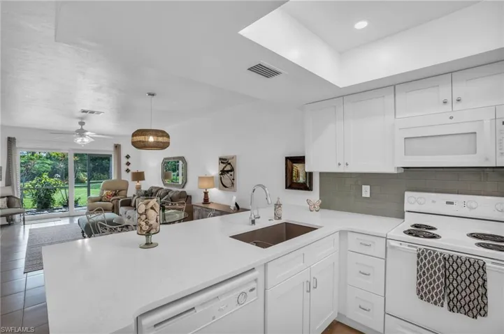 Kitchen featuring kitchen peninsula, ceiling fan, tasteful backsplash, sink, and white appliances