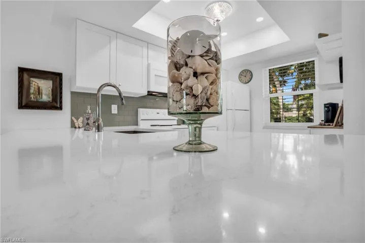 Kitchen with backsplash, a raised ceiling, light stone countertops, white cabinets, and white appliances