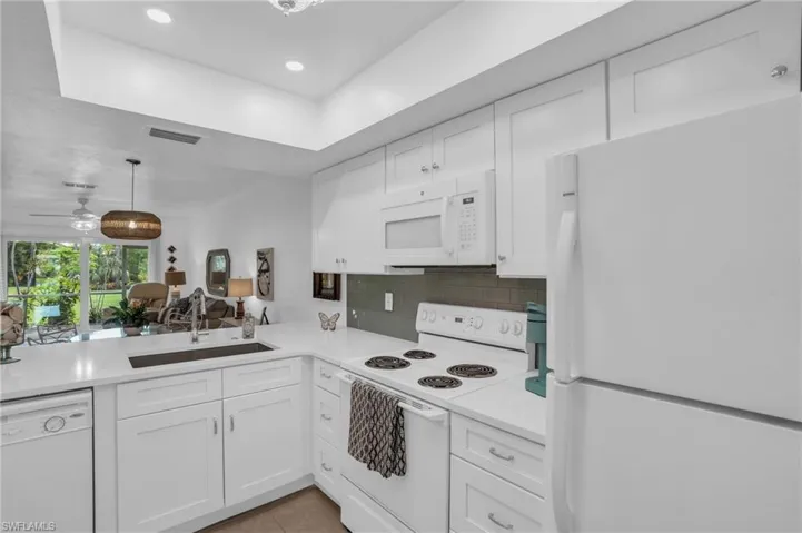 Kitchen with light tile flooring, backsplash, hanging light fixtures, white cabinetry, and white appliances