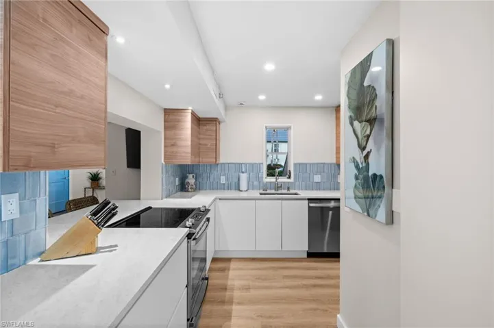 Kitchen with decorative backsplash, appliances with stainless steel finishes, light stone counters, light wood-style flooring, and modern cabinets