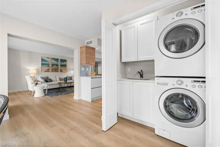 Laundry area with stacked washing machine and dryer, light wood-style floors, and cabinet space