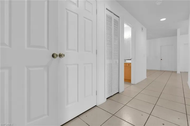 Hallway featuring light-toned tile flooring, recessed lighting, white paneled doors, and a louvered bifold door