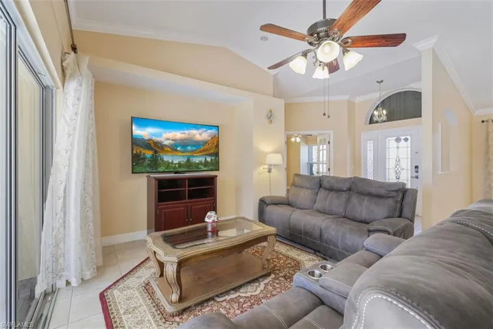 Living room featuring crown molding, vaulted ceiling, a ceiling fan, and light tile patterned floors
