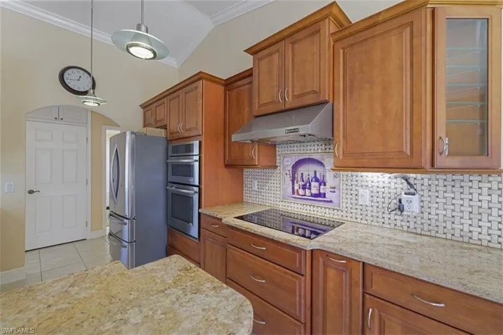 Kitchen featuring wood finish cabinets, stainless steel appliances, light stone countertops, pendant lighting, and ornamental molding