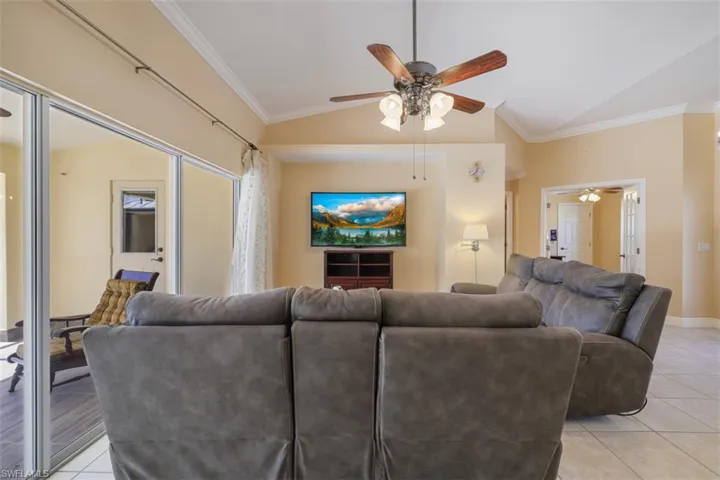 Living room with ornamental molding, light tile patterned floors, lofted ceiling, and a ceiling fan