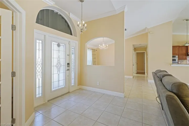 Foyer with a chandelier, crown molding, vaulted ceiling, and light tile patterned flooring
