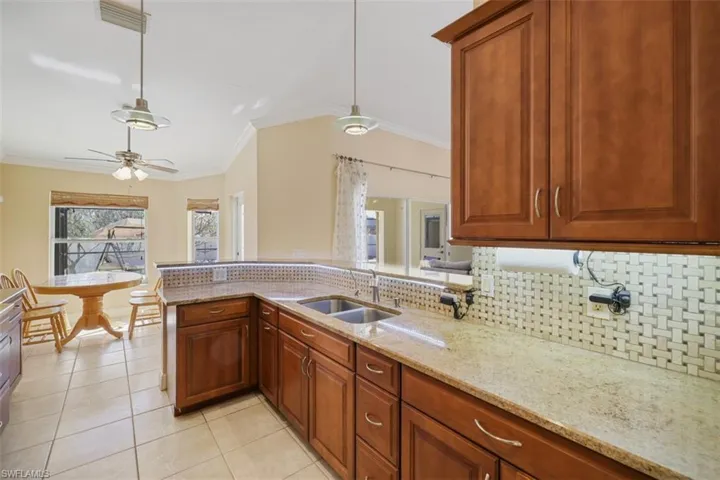 Kitchen with ornamental molding, light stone counters, pendant lighting, backsplash, and wood finish cabinetry